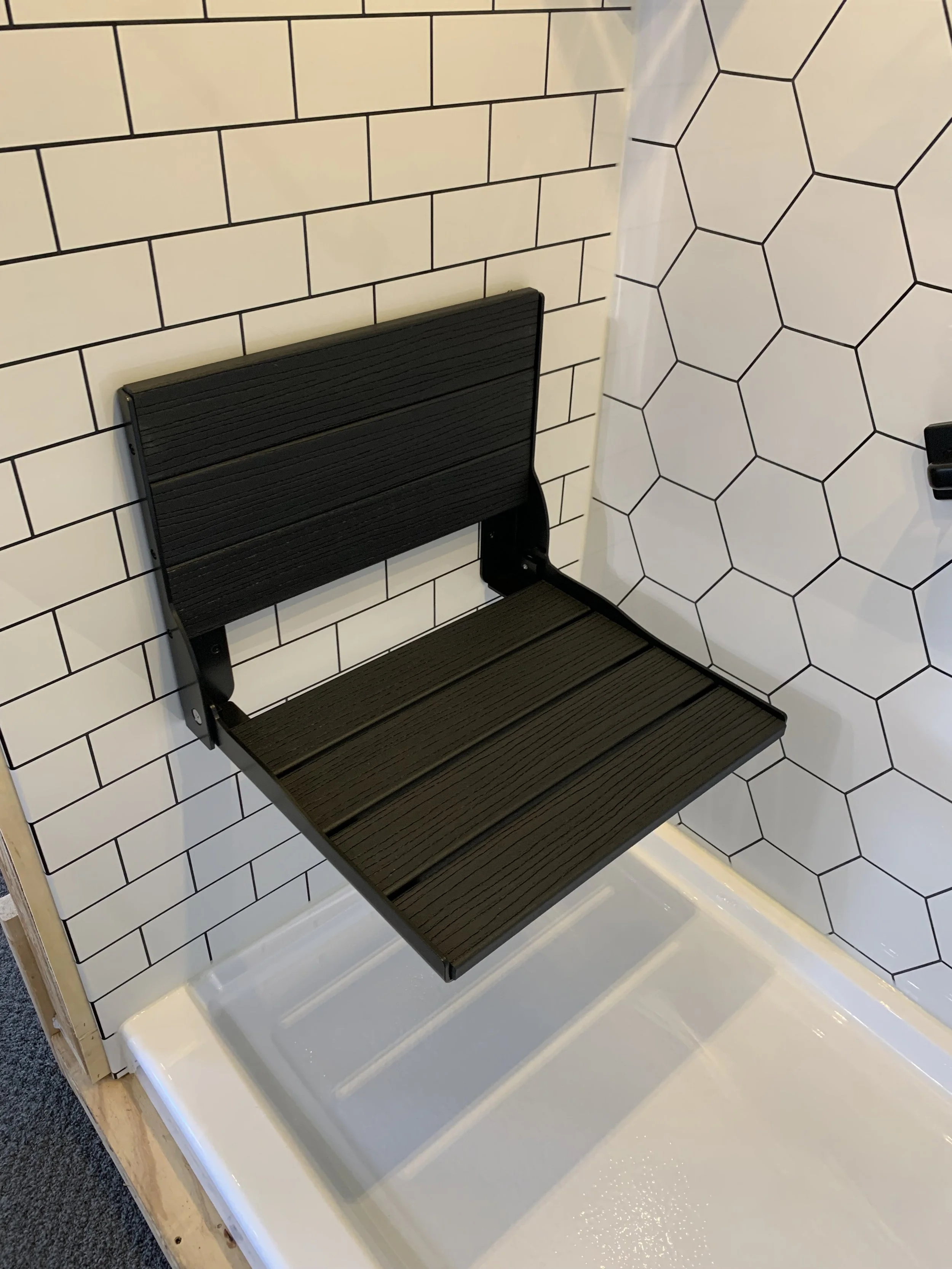 Display of black shower benches with a white tiled wall background.