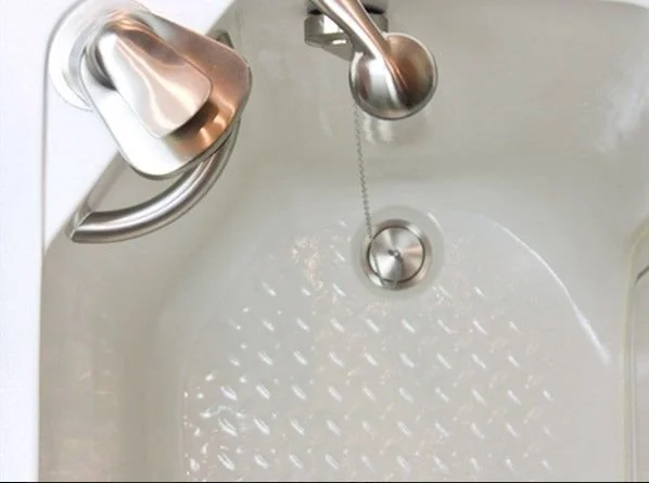 Empty white bathtub with a silver handheld showerhead on a chain and a tea kettle sitting on the edge.