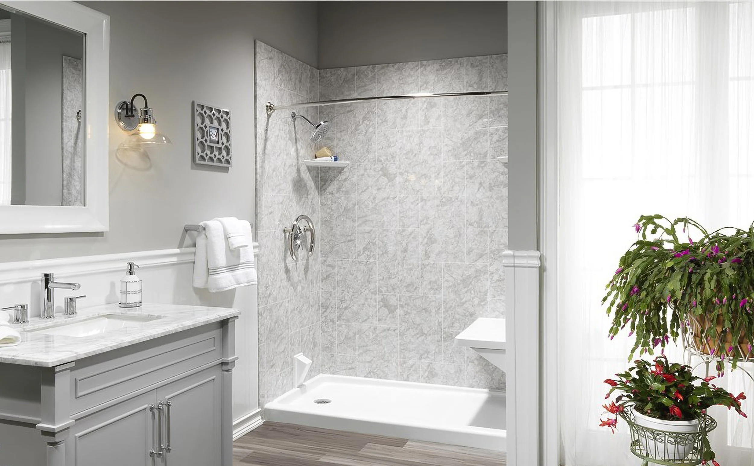 A modern bathroom with a shower area, a white vanity with a marble countertop, a mirror, plants, and soft natural lighting.