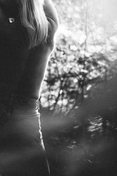 Schwarz-weiß-Foto einer Person, die nur den Rücken zeigt, mit langen Haaren, vor einem unscharfen natürlichen Hintergrund.