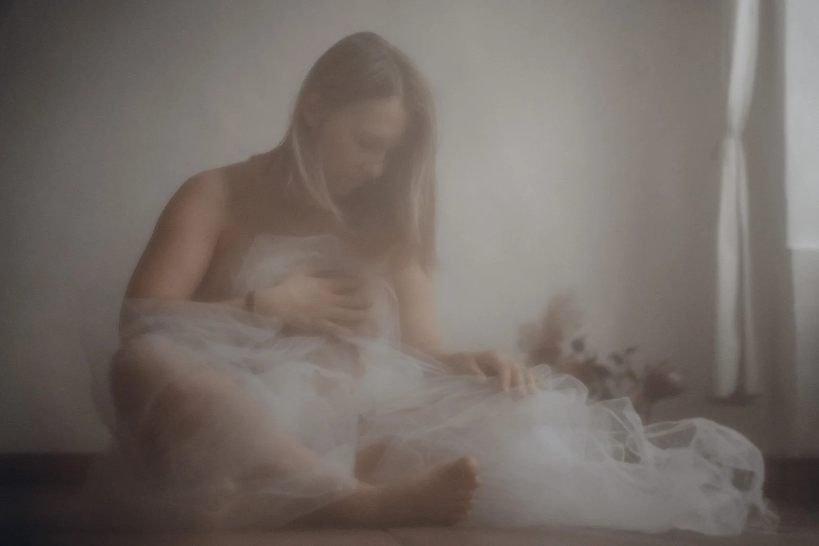 Eine Frau in einem weißen Kleid sitzt auf dem Boden, umgeben von Nebel oder Rauch, in einem hell erleuchteten Raum.