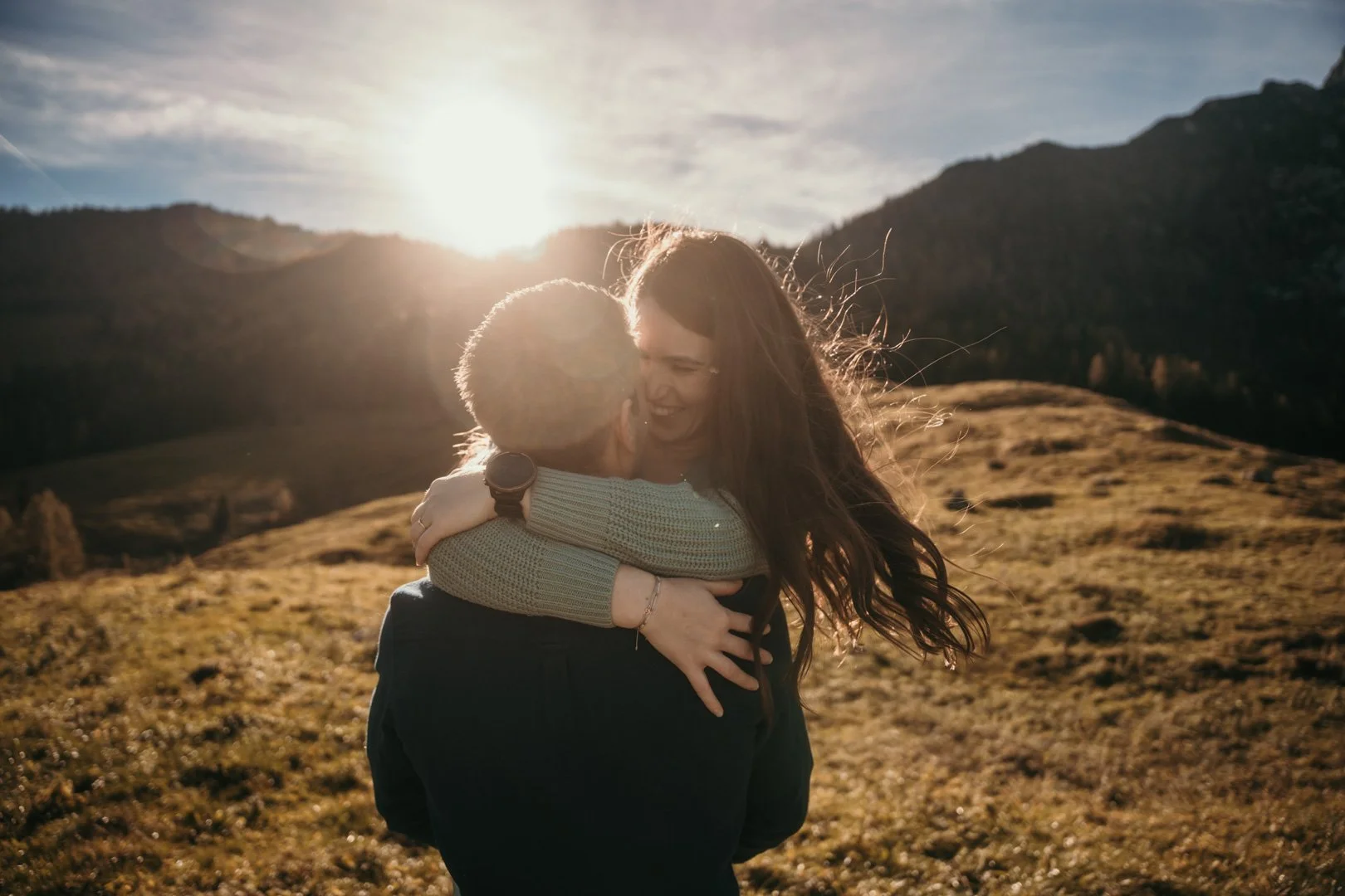 Zwei Menschen umarmen sich in einer Berglandschaft bei Sonnenuntergang.