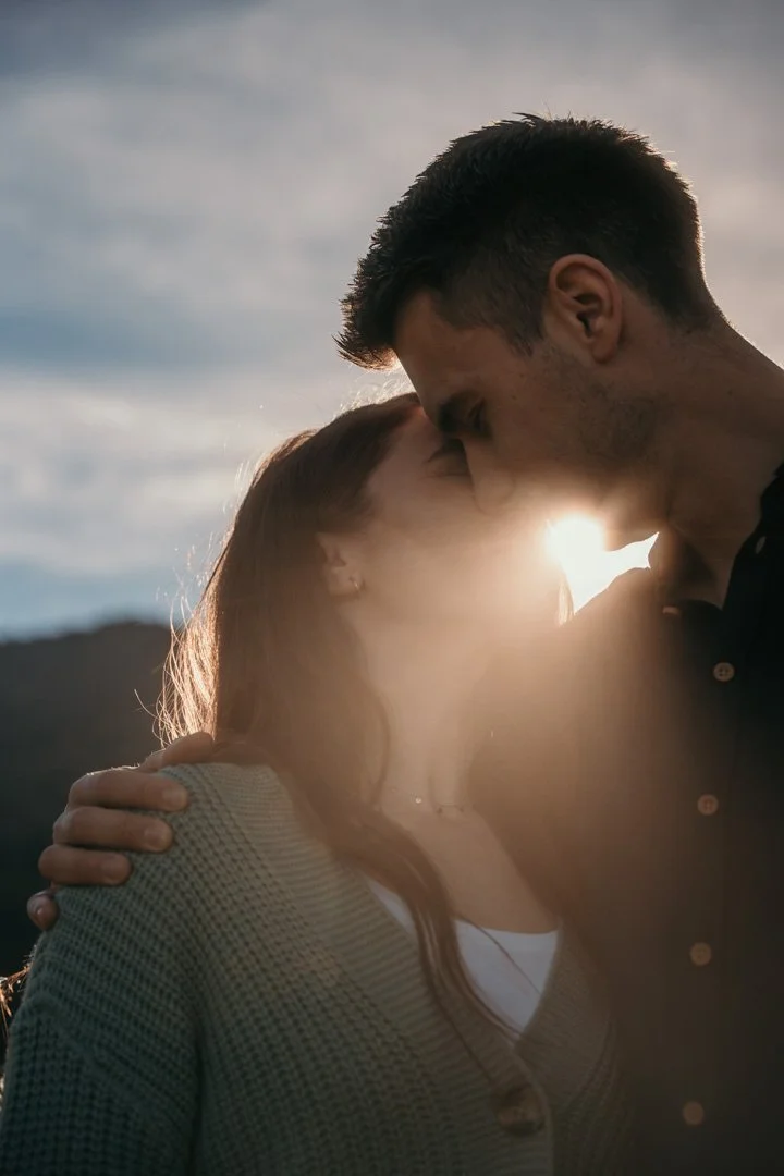 Ein Mann und eine Frau küssen sich im Sonnenuntergang im Freien.