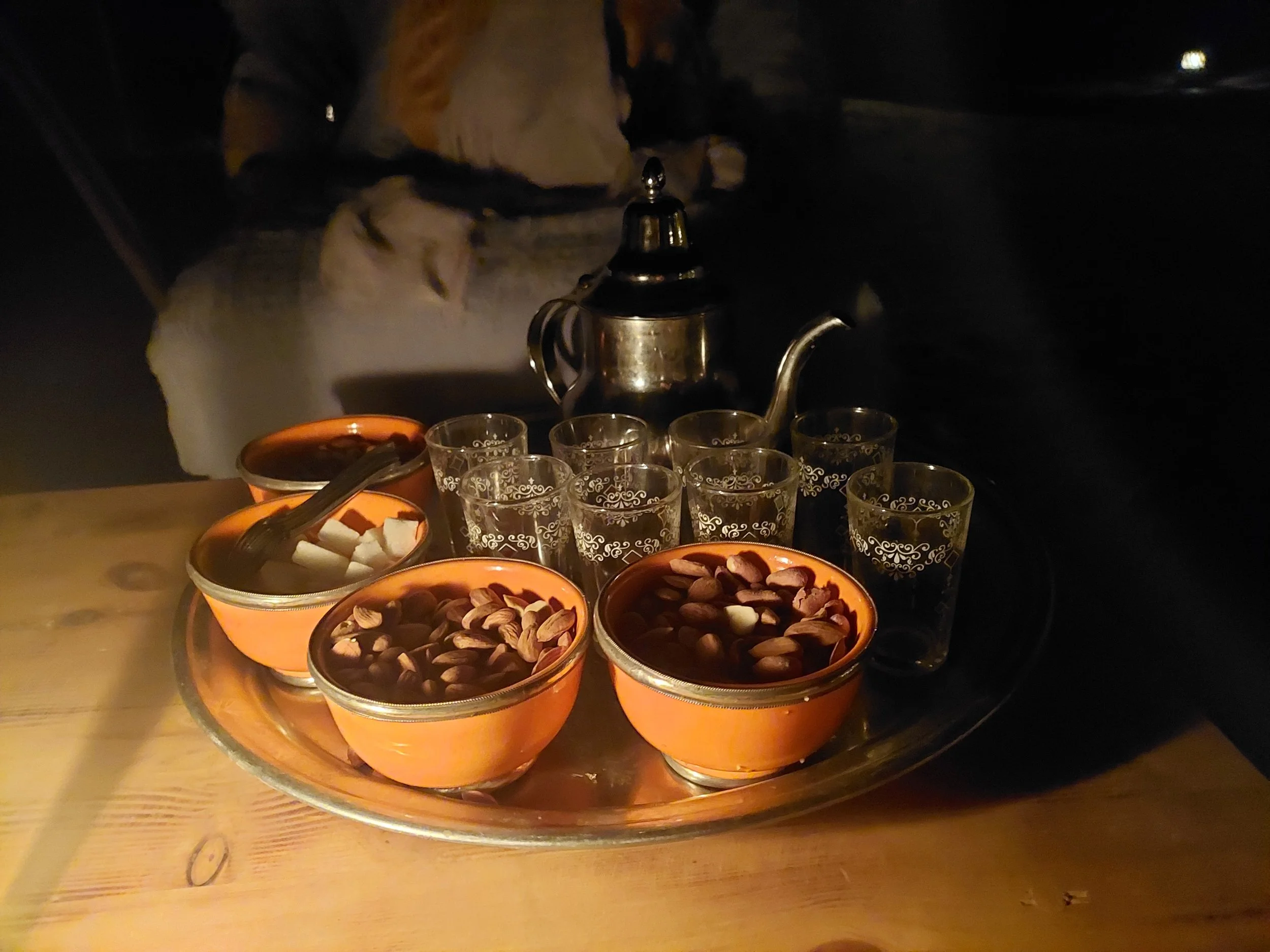 Eine Edelstahl Teekanne, vier Gläser mit Arabischem Kaffee, Schalen mit Zuckerwürfeln, Mandeln und Pistazien, auf einem runden Silbertablett.