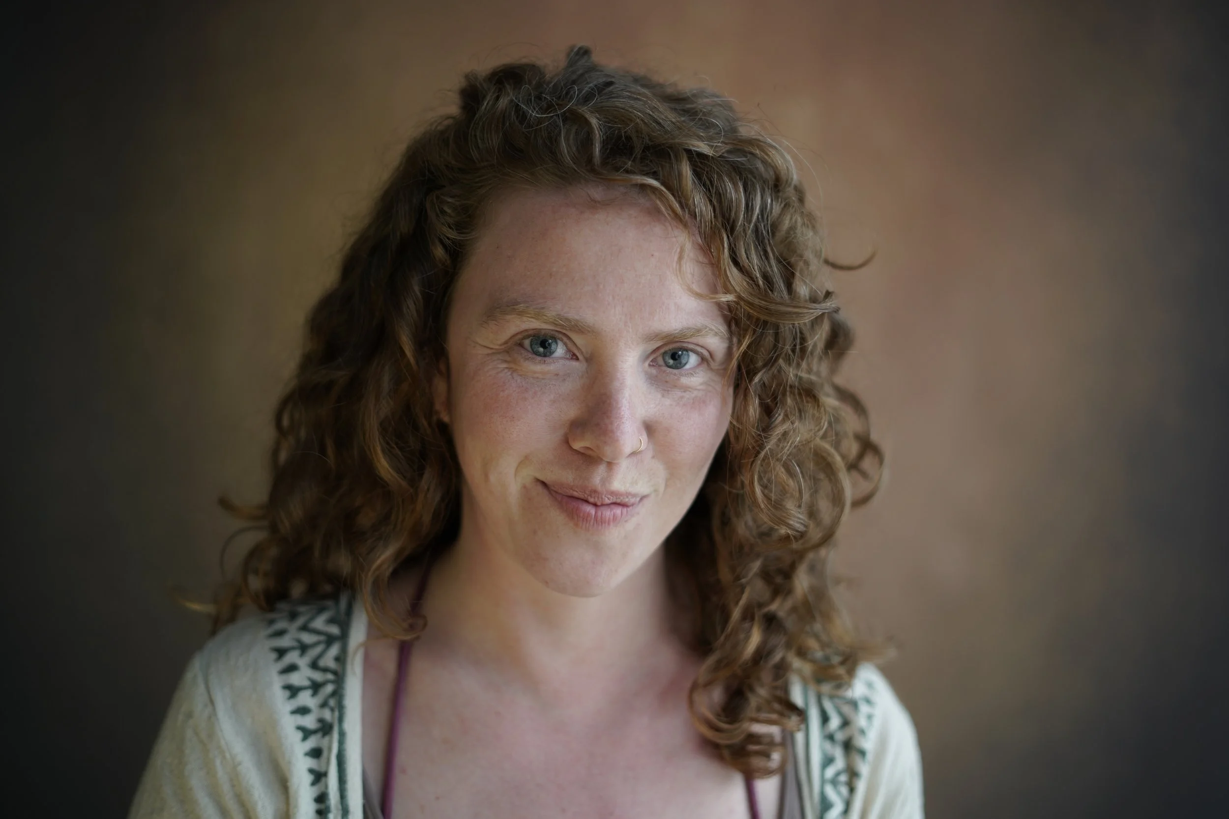 Nahaufnahme eines lachenden roten-haired Mädchens mit blauen Augen und Sommersprossen, trägt ein weißes Kleid mit grünen Mustern an den Schultern, dunklem Hintergrund.