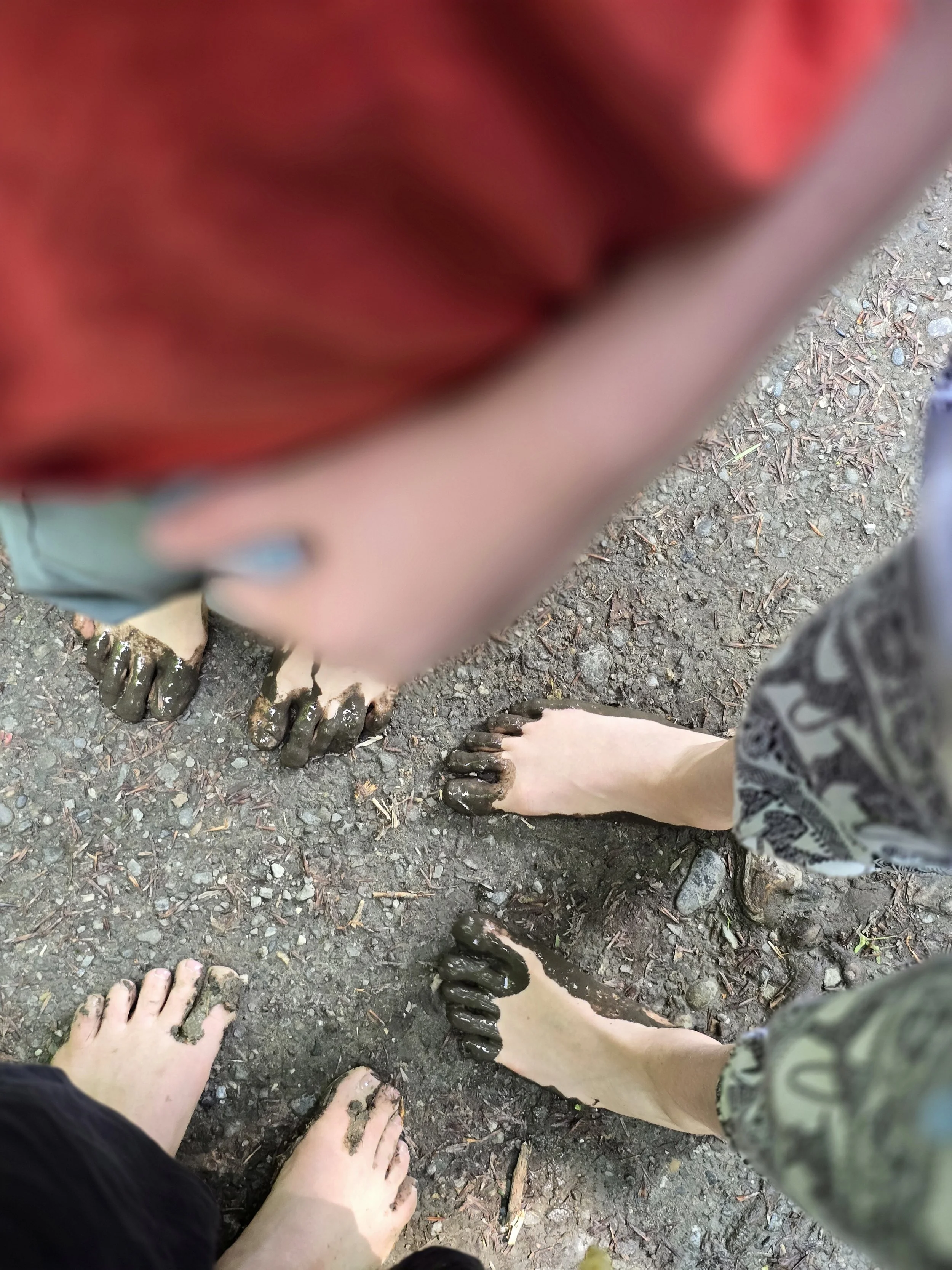 Füße von mehreren Personen, die barfuß im Schlamm stehen.