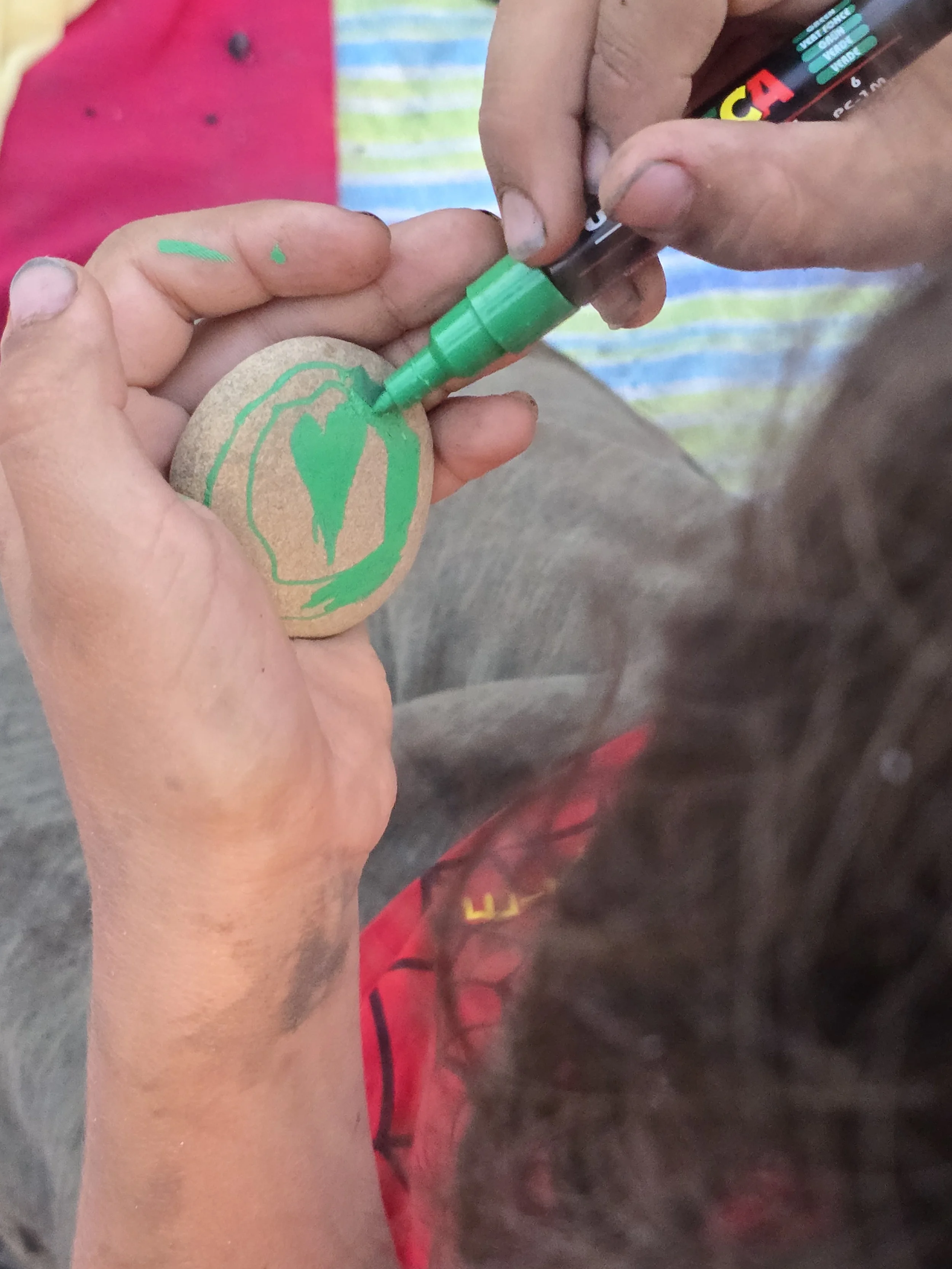 Jemand malt mit einem grünen Marker auf einem Stein, während eine andere Person den Marker benutzt.
