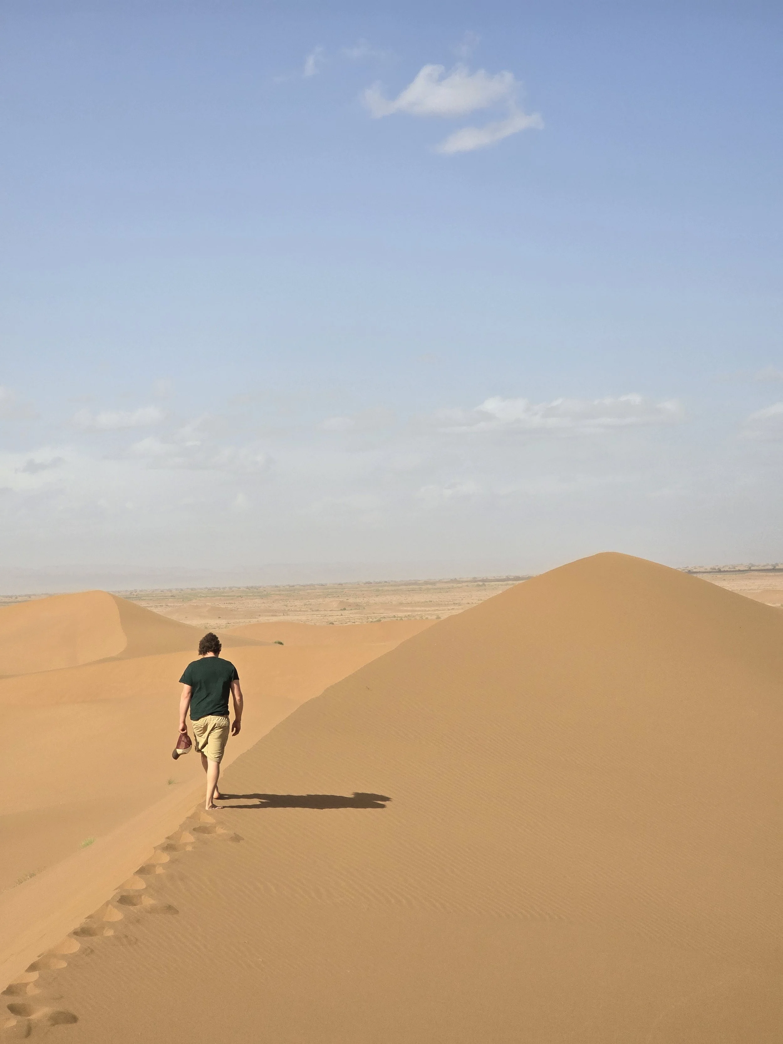 Ein Mann wandert auf einer Sanddüne in einer Wüste unter blauem Himmel mit einigen weißen Wolken.