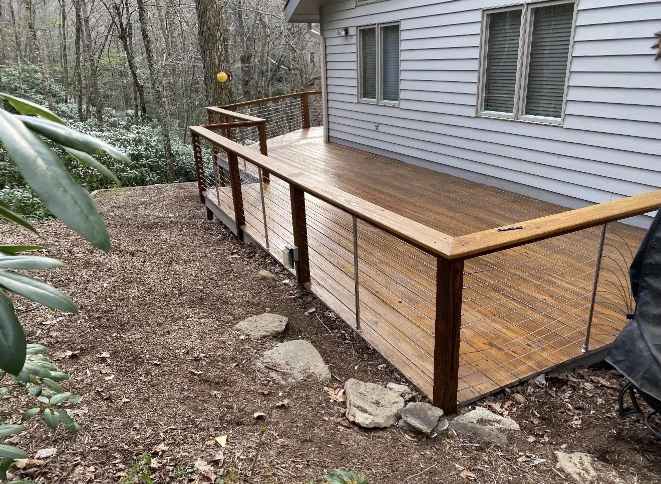 Wooden deck with metal railings attached to a house in a wooded backyard, built by Antonio's Construction serving Ashe and Watauga County in North Carolina.