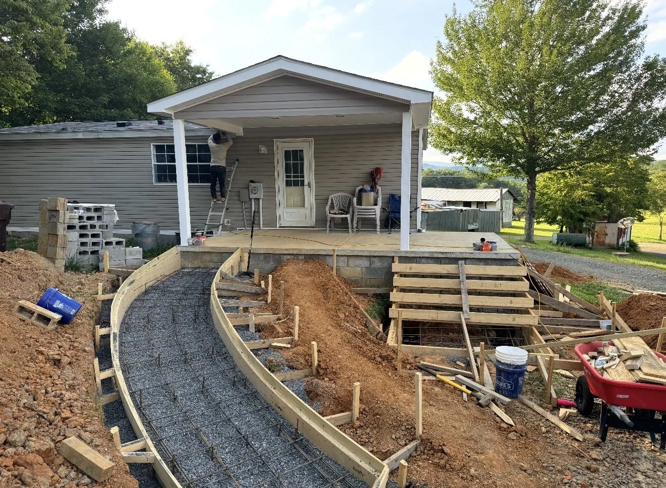 Construction workers building a curved concrete walkway in front of a house, with stairs leading up to the porch,  by Antonio's Construction serving Ashe and Watauga County in North Carolina.