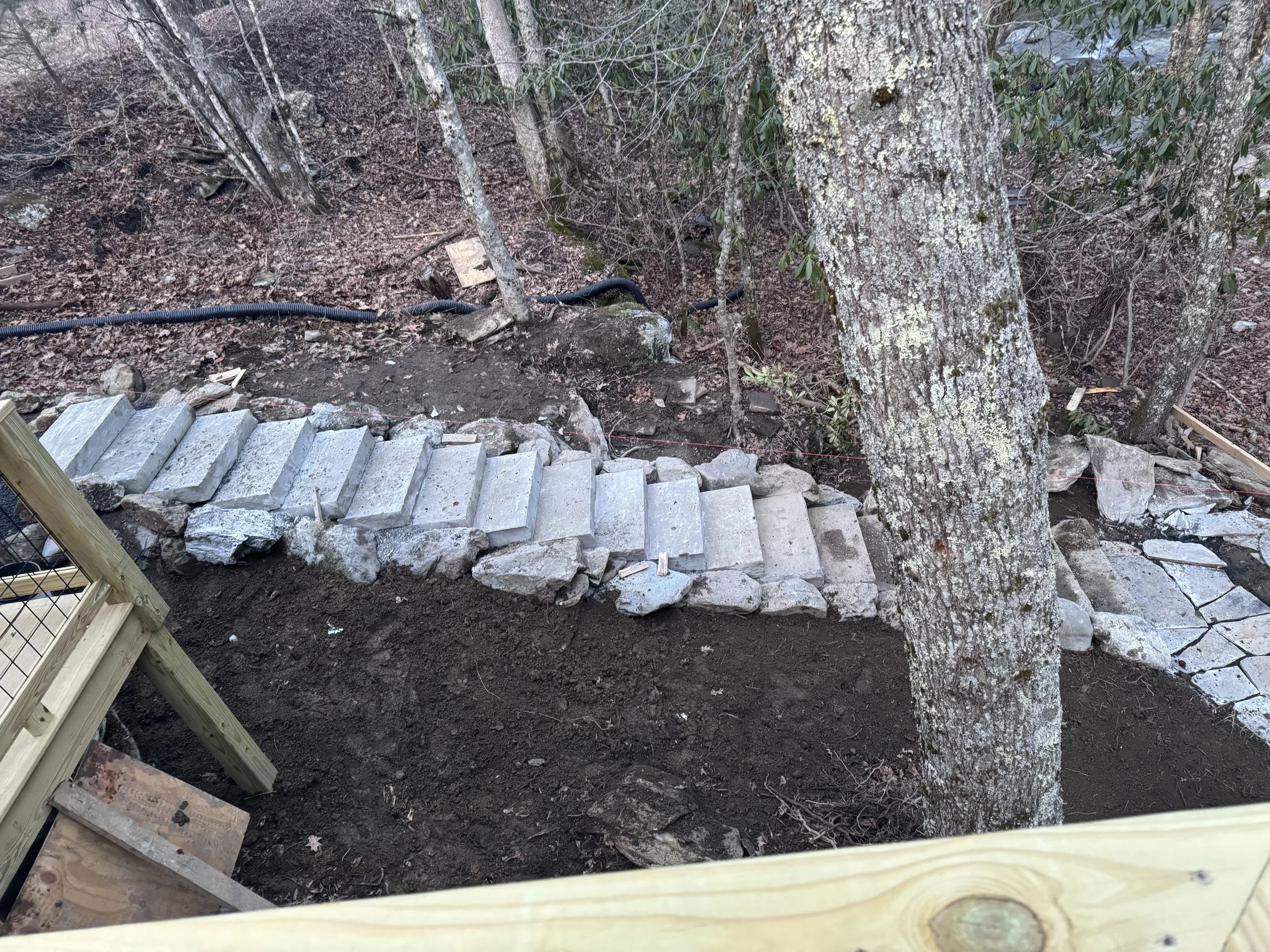Construction of a stone pathway around a tree in a wooded area, with wooden framing by Antonio’s Construction providing exterior construction in Ashe County and Watauga County, NC