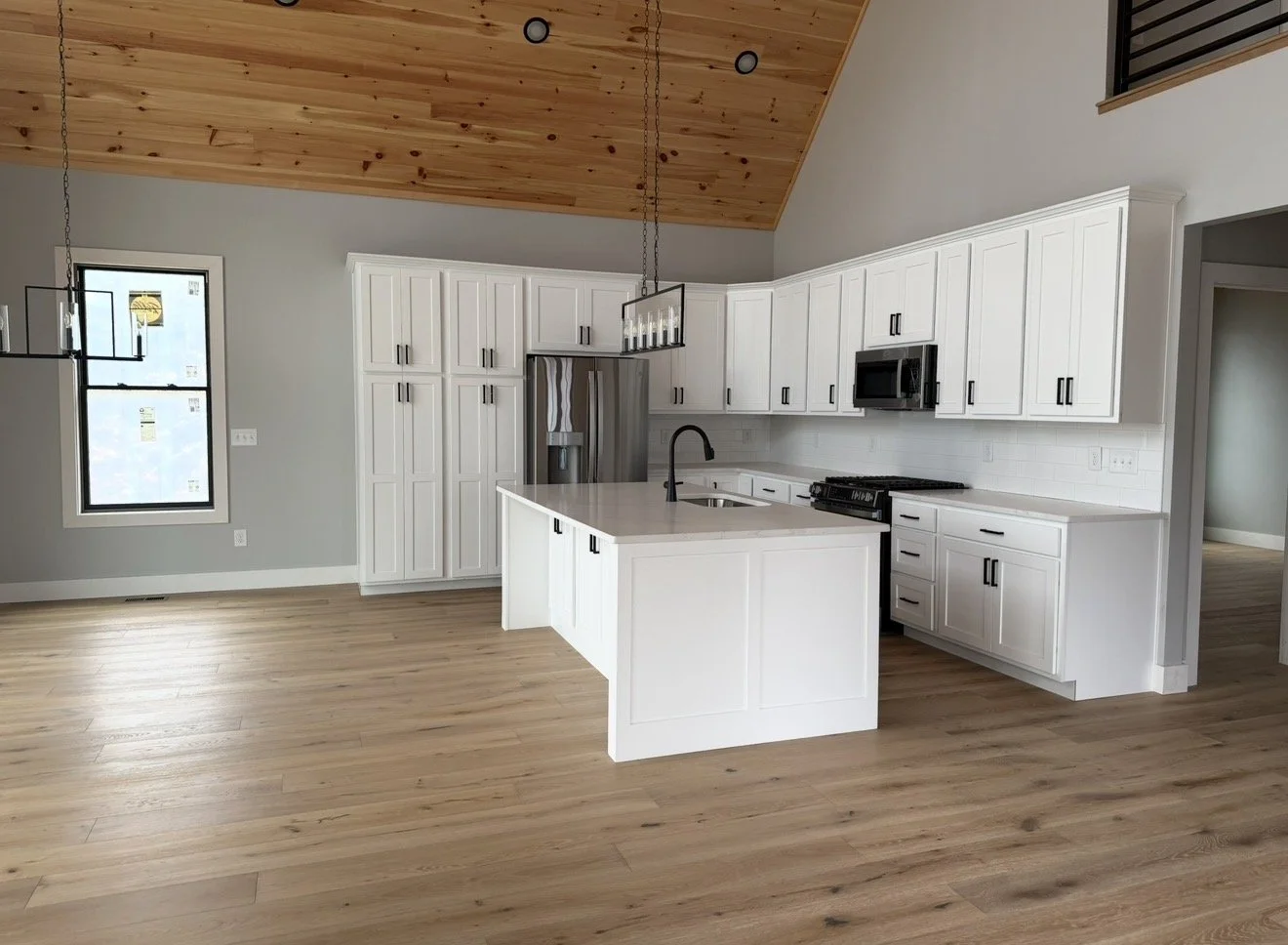 Modern kitchen with white cabinets, a kitchen island with a black faucet, gray walls, wooden ceiling, and hardwood floors.