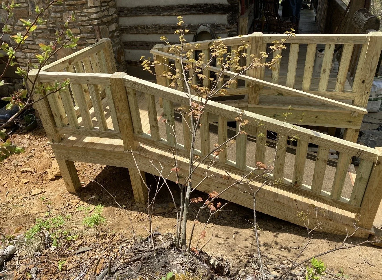 A wooden ramp with railings leading to a wooden deck outside a rustic house. Built by Antonio's Construction serving Ashe and Watauga County in North Carolina.