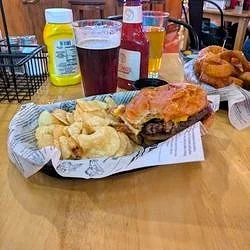 A meal with a burger and fries on a paper-lined tray, two glasses of dark soda, and condiments on a restaurant table.