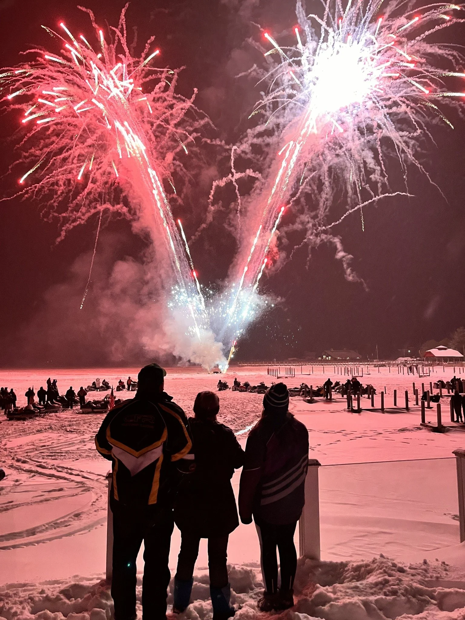 People watching fireworks display over snowy ground at night.