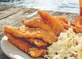 Plate of fried fish fillets with coleslaw and tartar sauce on a wooden table.