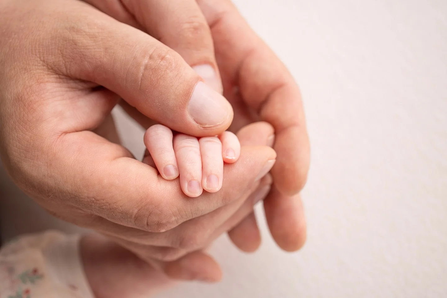 A close-up of an adult's hand holding a tiny baby's hand.