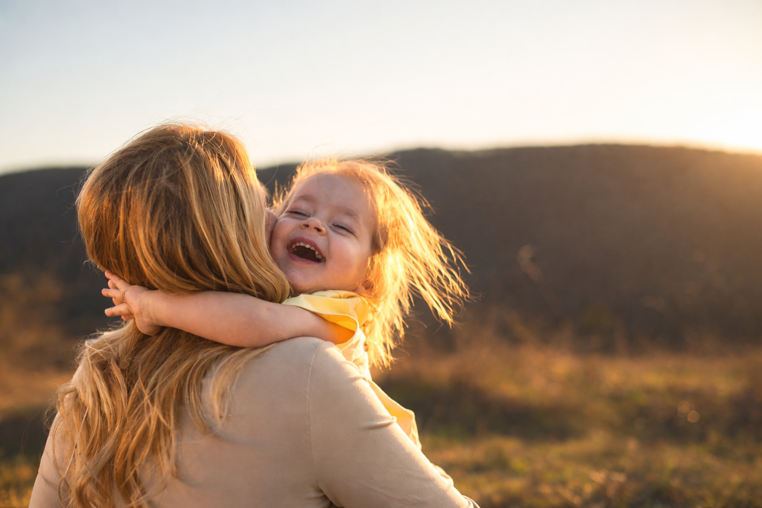 A woman holding a smiling red-haired girl outdoors during sunset.