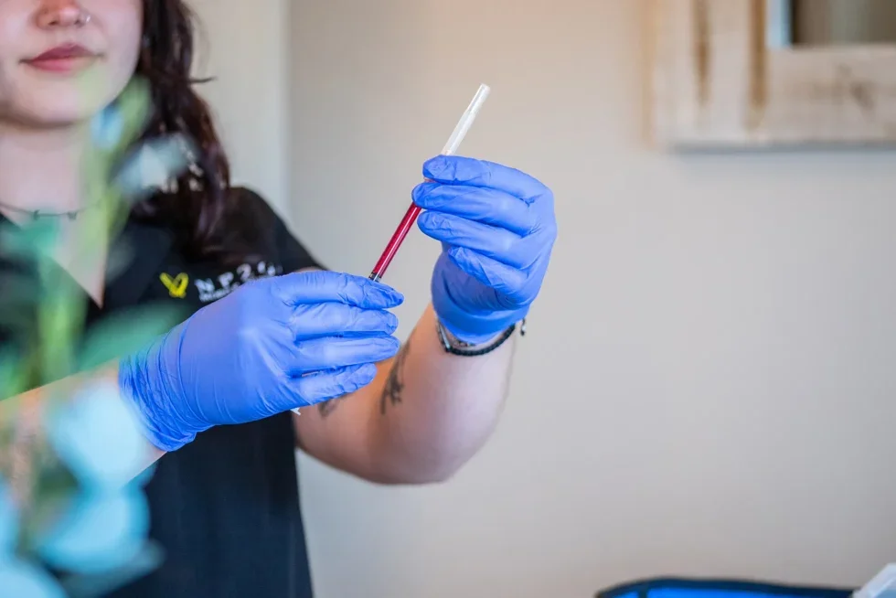 A person wearing blue gloves handling a test tube with a red liquid.