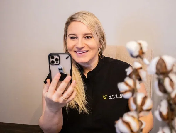 A woman smiling and using a smartphone, with a blurred plant in the foreground.