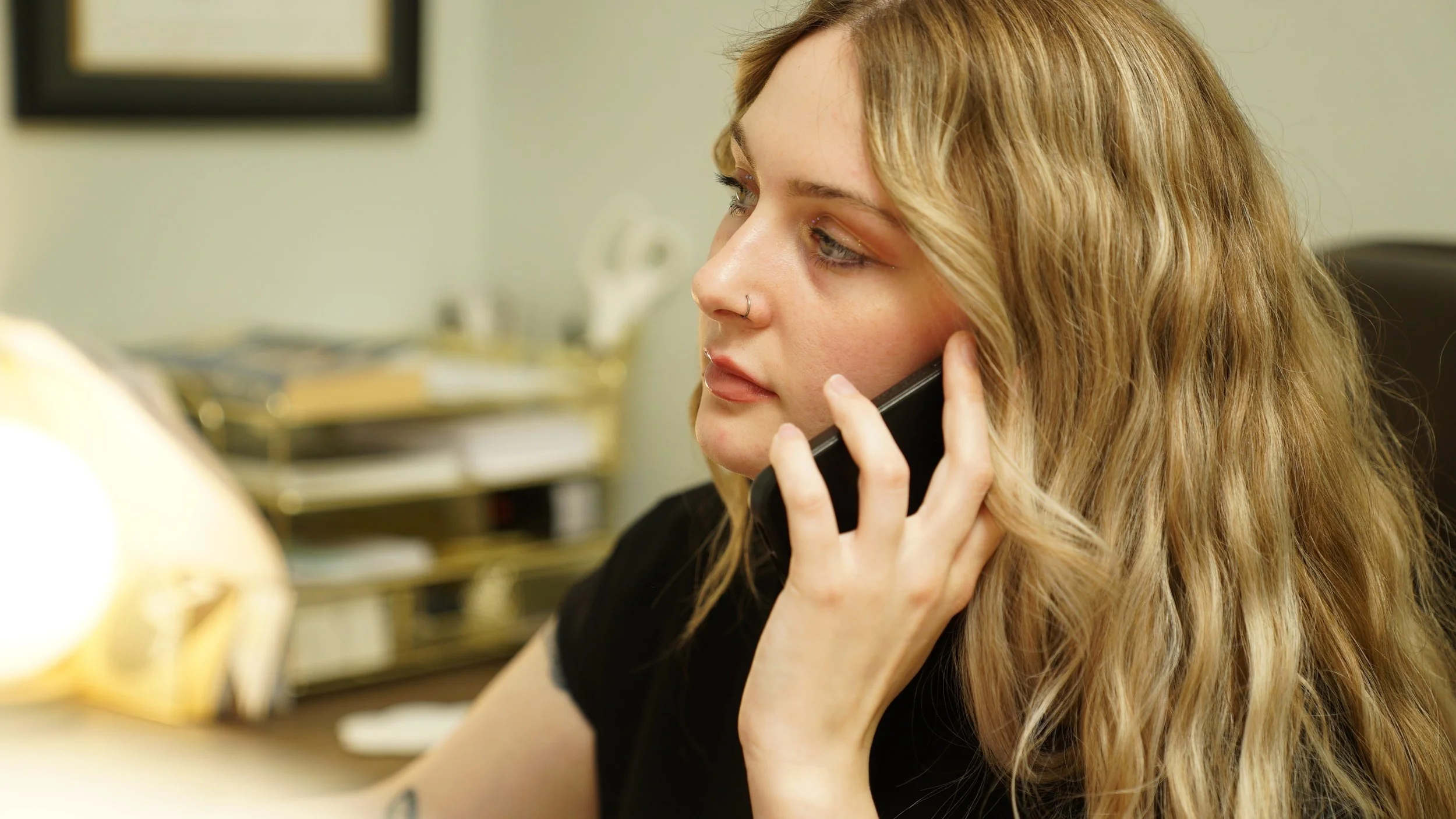 Young woman with long blonde hair and nose rings talking on the phone in an office setting