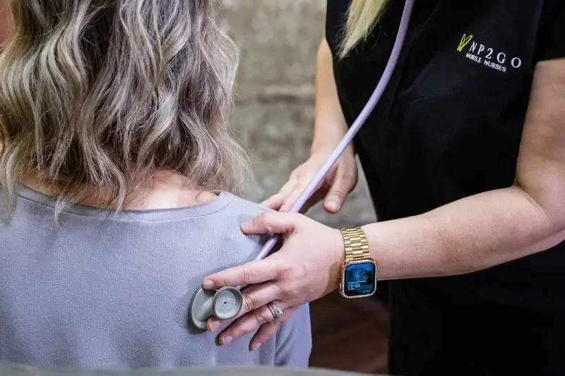 A healthcare professional is checking a patient's heartbeat with a stethoscope on her back at a medical setting.