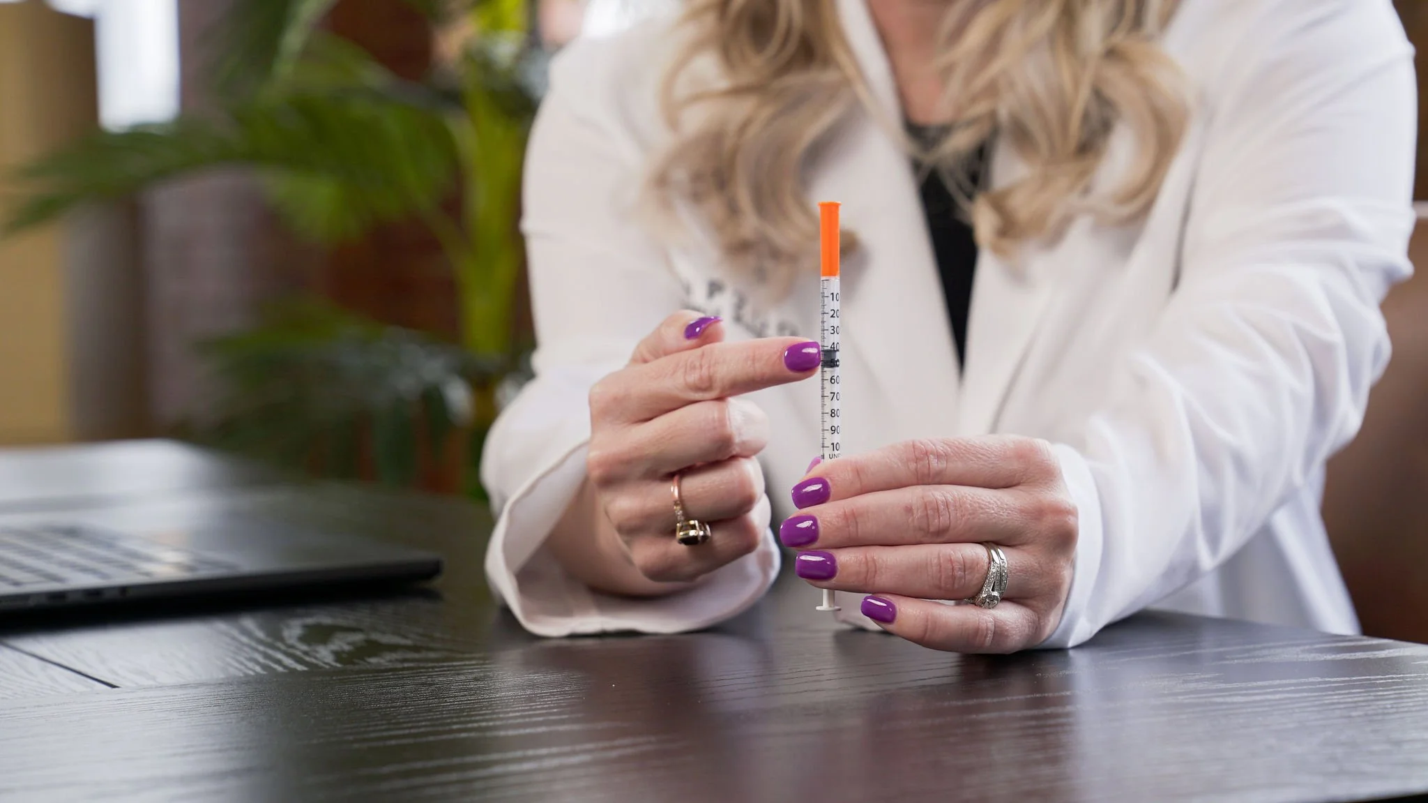 Person with purple nails holding a syringe with an orange plunger in a professional setting.