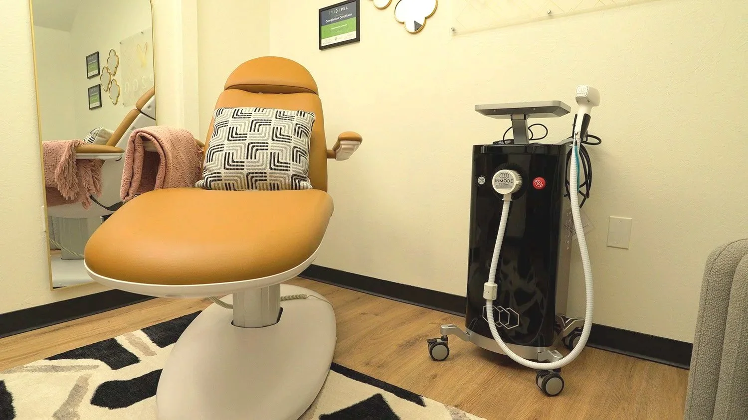 Medical exam room with a reclining chair, pink towels, and medical equipment including a black cart with hoses and monitors.