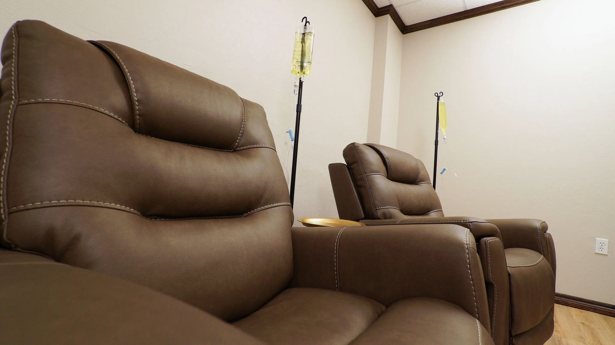 Hospital waiting room with brown leather chairs and IV poles with yellow fluids.