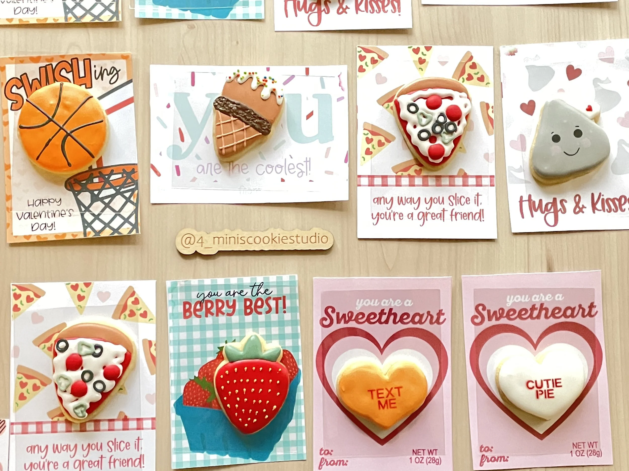 Set of decorated cookies and cards with Valentine's Day and friendship messages. Includes a basketball cookie, ice cream cone cookie, pizza slice cookie, smiling heart cookie, strawberry cookie, and two heart cookies with text.