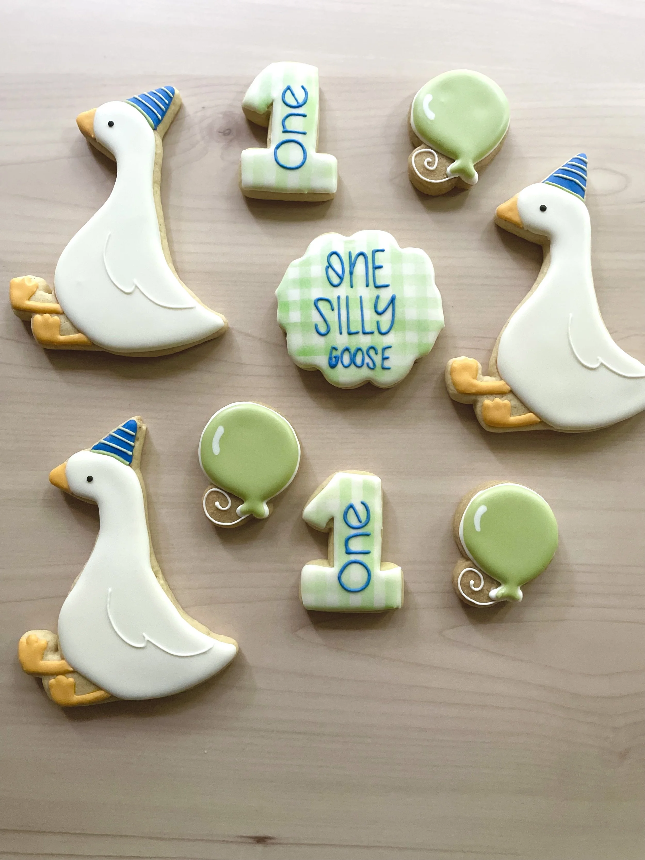 Decorated cookies celebrating a first birthday, including swan cookies, balloon cookies, and cookies with messages 'One' and 'One Silly Goose.'