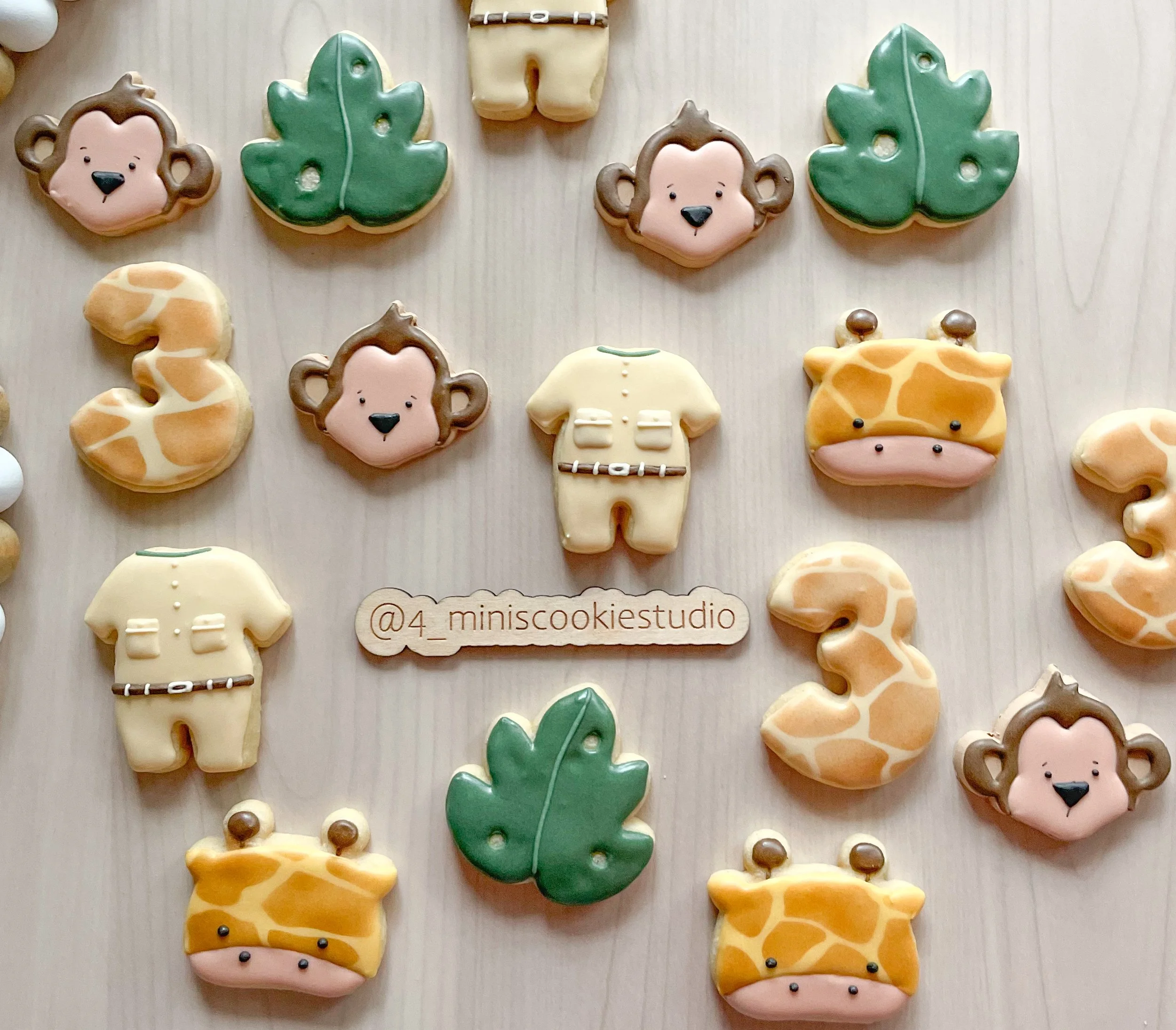 Decorative animal-shaped cookies, including monkeys, giraffes, and leaves, arranged on a light wooden surface with an Instagram handle in the center.