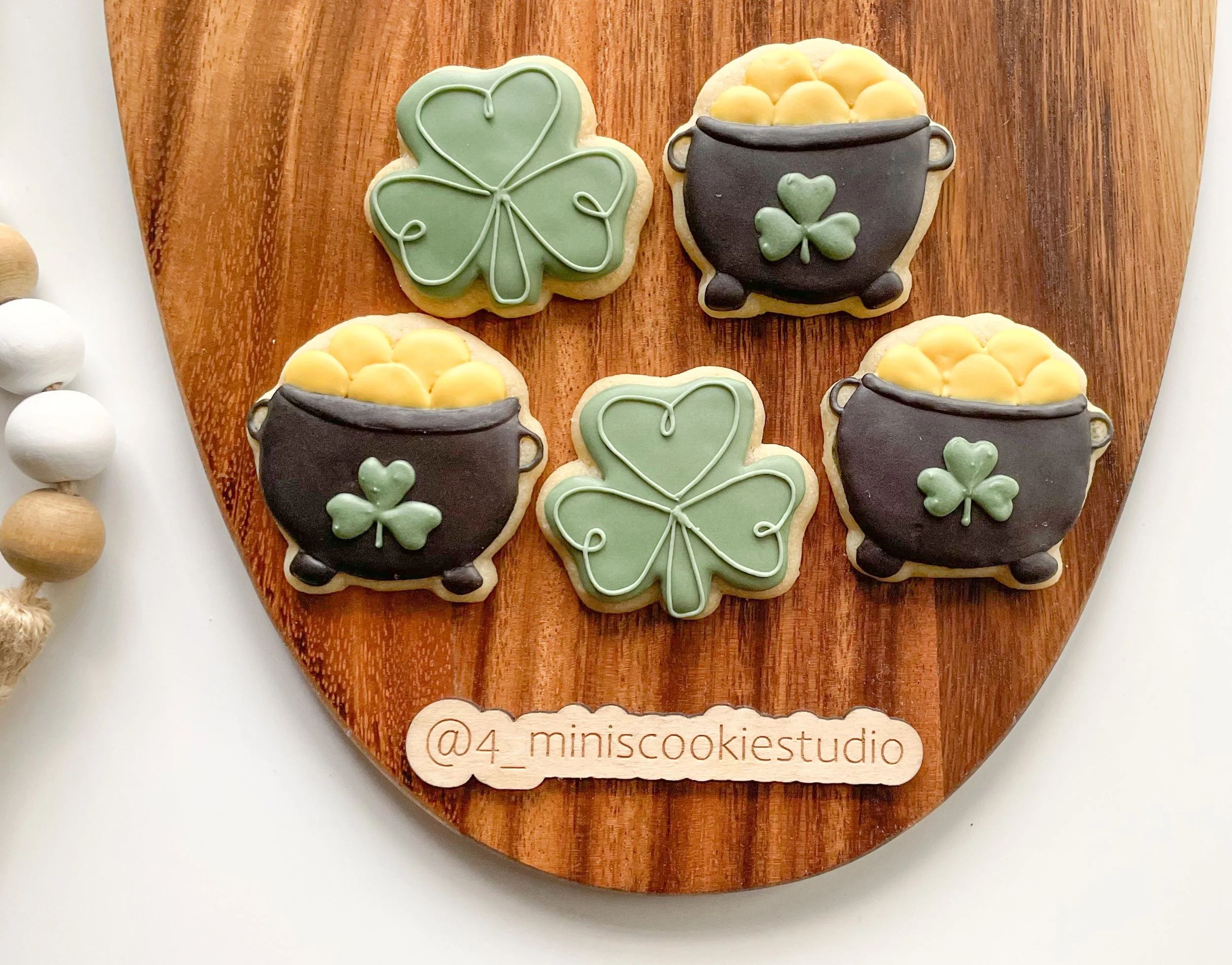 Cookies decorated with St. Patrick's Day theme, including four pots of gold and two shamrock-shaped cookies, arranged on a wooden board.