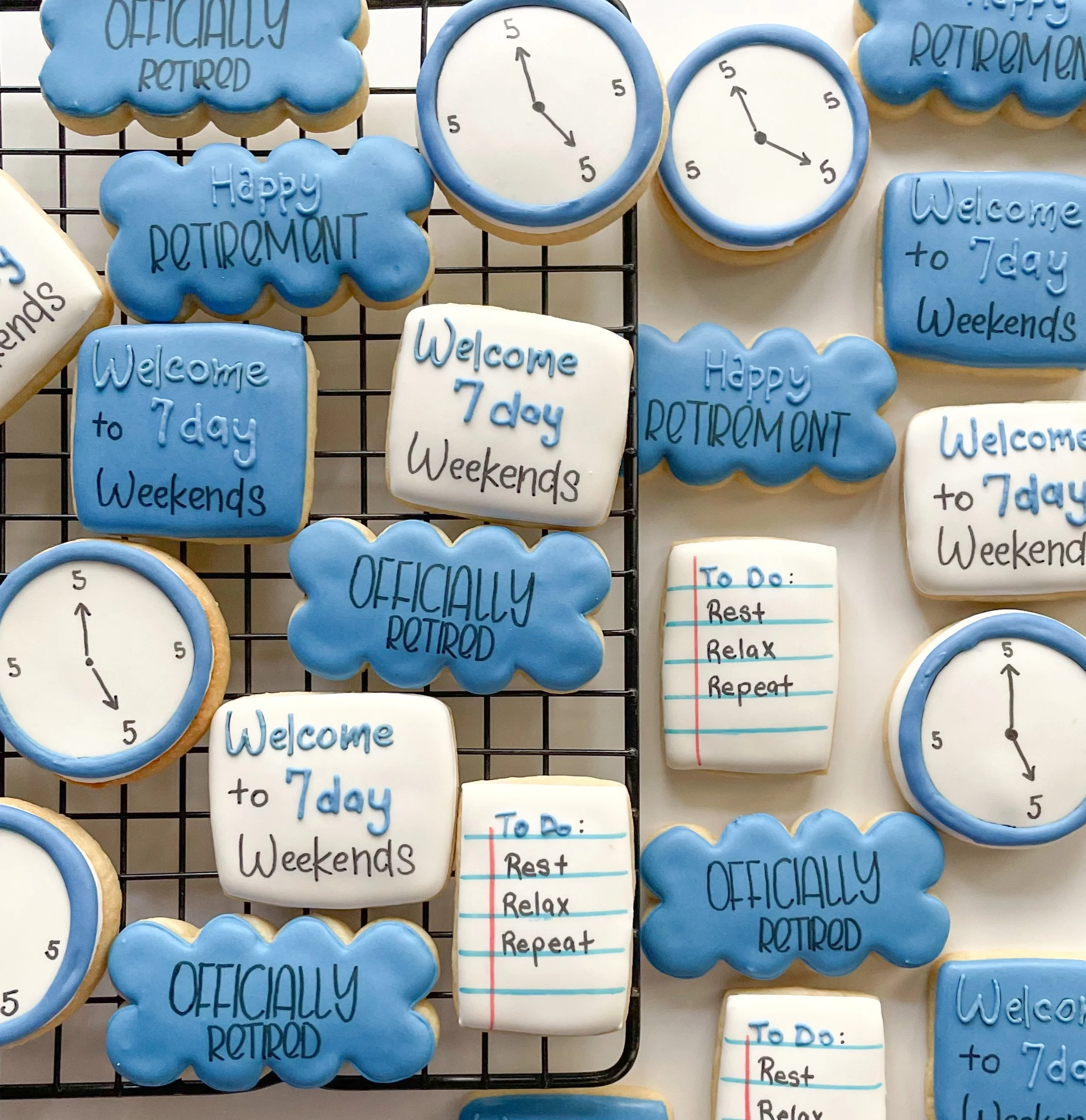 Cookies decorated with retirement and welcome messages, with clock designs and a to-do list, arranged on a black wire grid and a white surface.