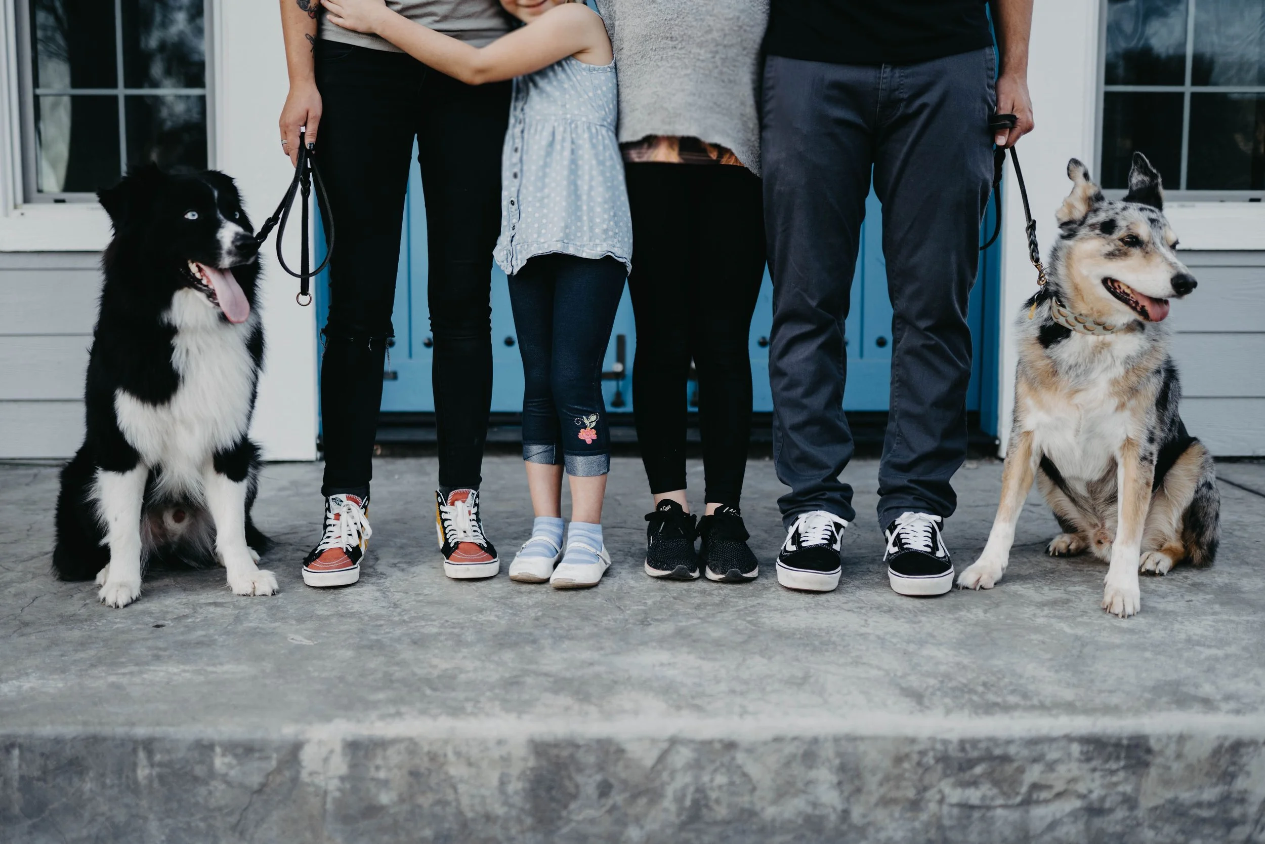 Family of three with two dogs standing on porch in front of house.
