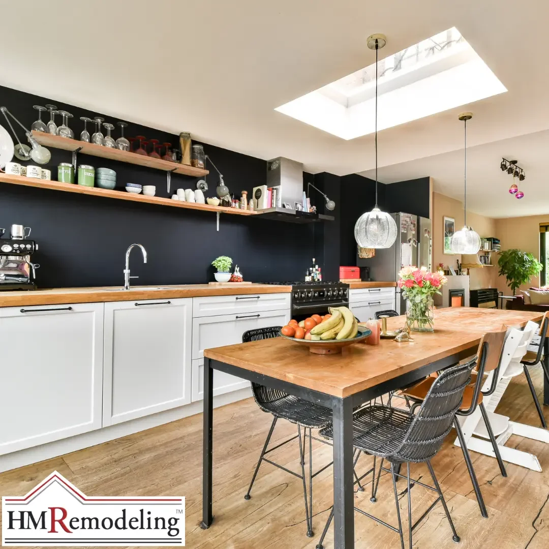 An open-concept kitchen with white cabinets, a black accent wall, open wood shelving, and a wood dining table with seating in a Michiana area home.