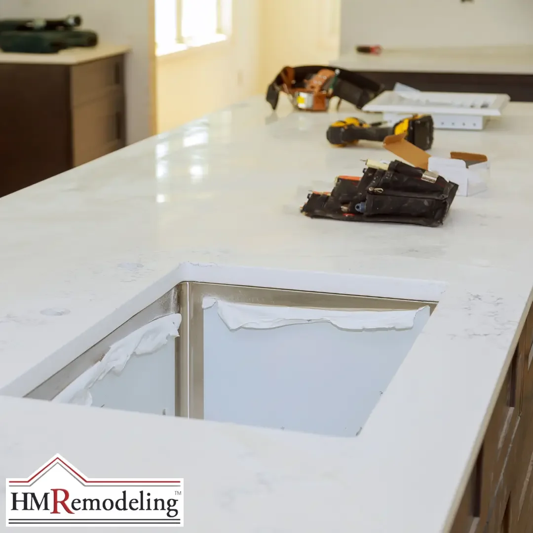 Close-up of a white quartz countertop with veining and an undermount stainless steel sink being installed during a kitchen remodel in South Bend, Indiana, with tools resting on the surface