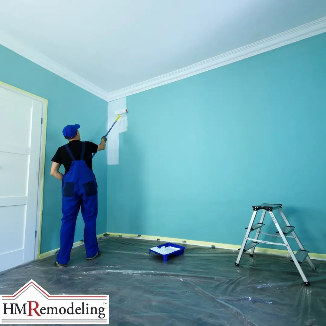 A painter in blue overalls rolling white paint onto a teal wall near crown molding in a South Bend, Indiana room, with a paint tray and ladder visible on a plastic-covered floor