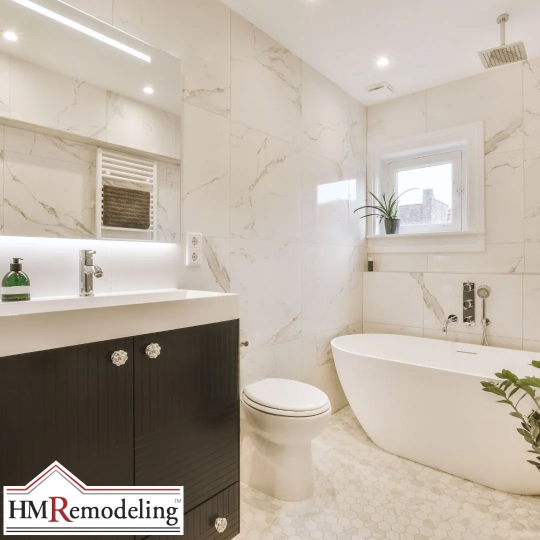Freestanding soaking tub, large format marble wall tile, LED backlit vanity mirror, and dark wood cabinetry in a South Bend, Indiana bathroom remodel by HM Remodeling