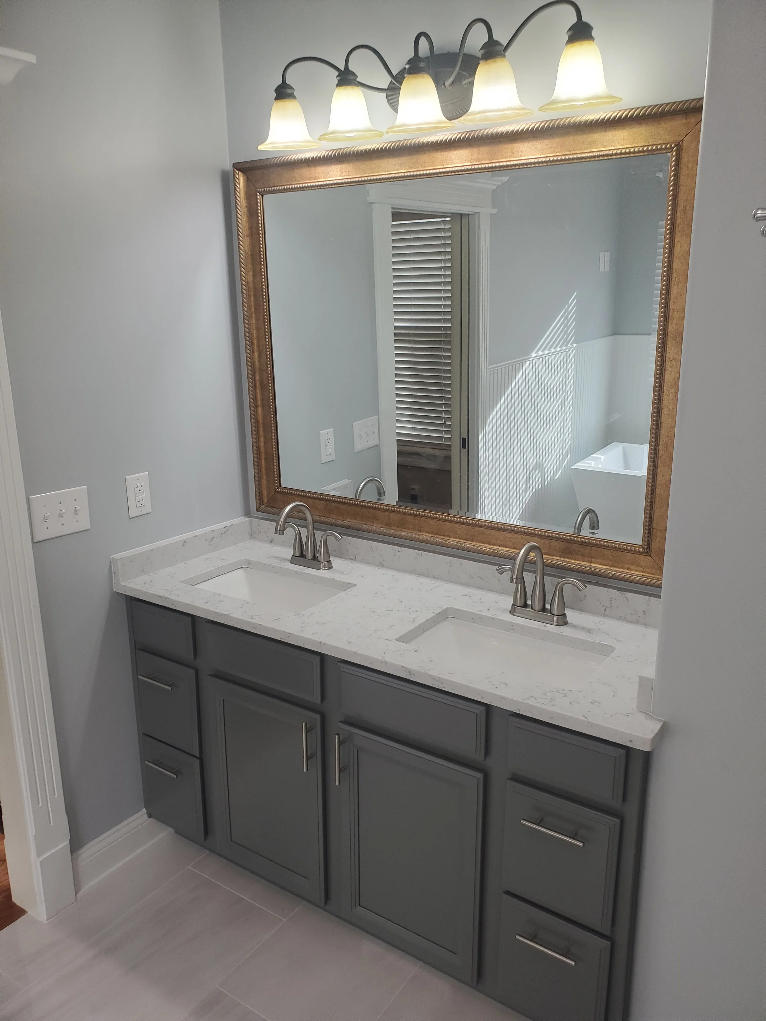 HM Remodeling bathroom remodel featuring wood frame mirror warm sconce lighting and marble countertop in South Bend Indiana