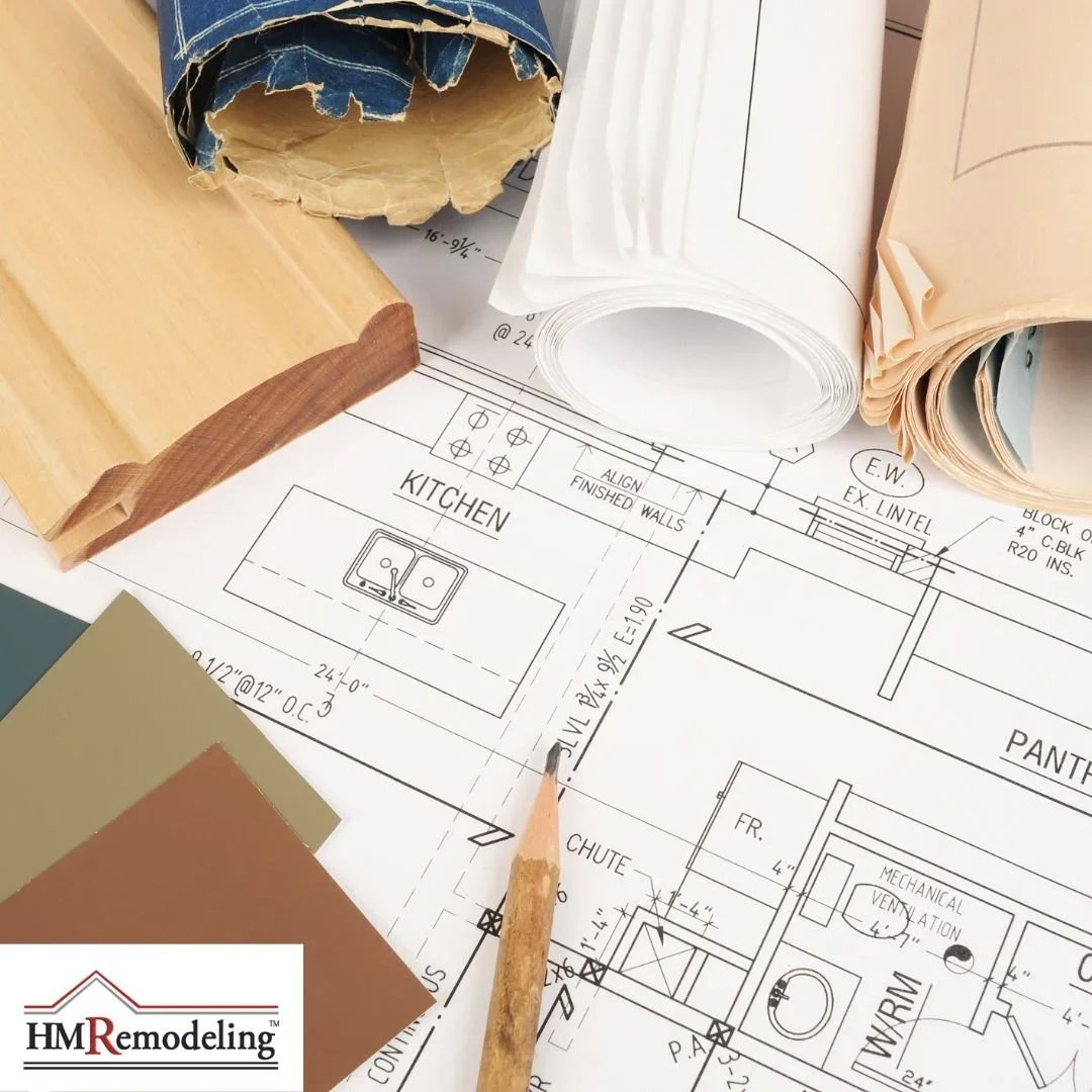 Home remodeling plans and blueprints spread on work surface with wood trim samples, color swatches, rolled plans, and pencil by HM Remodeling in South Bend, Indiana