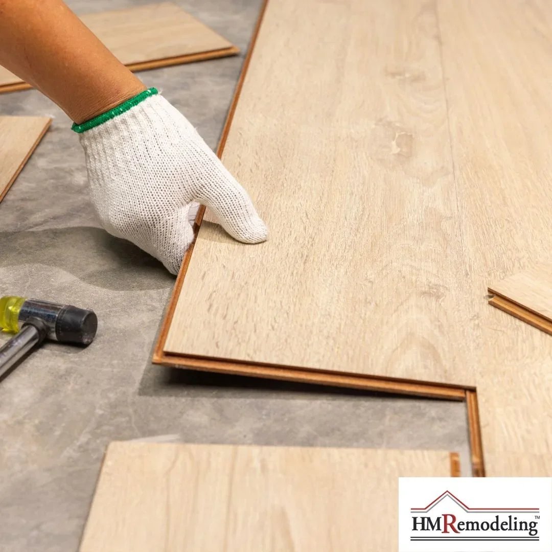 Hardwood flooring installation with gloved installer fitting light oak laminate planks over underlayment with rubber mallet nearby by HM Remodeling in South Bend, Indiana