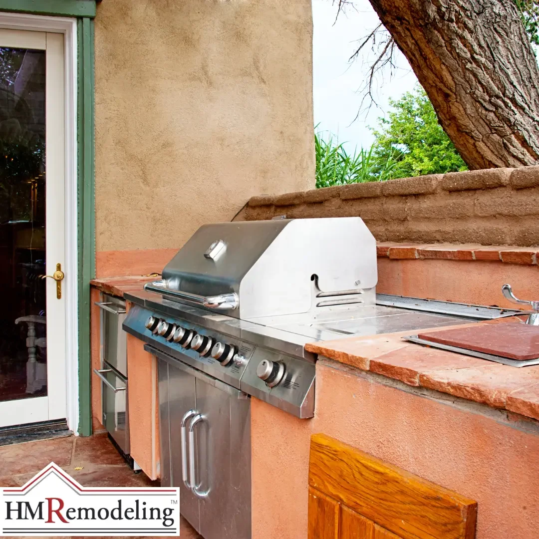 A built-in outdoor grill station with a stainless gas grill, storage drawers, and stone-tiled counters against a stucco wall, an outdoor kitchen example for a South Bend, Indiana home.