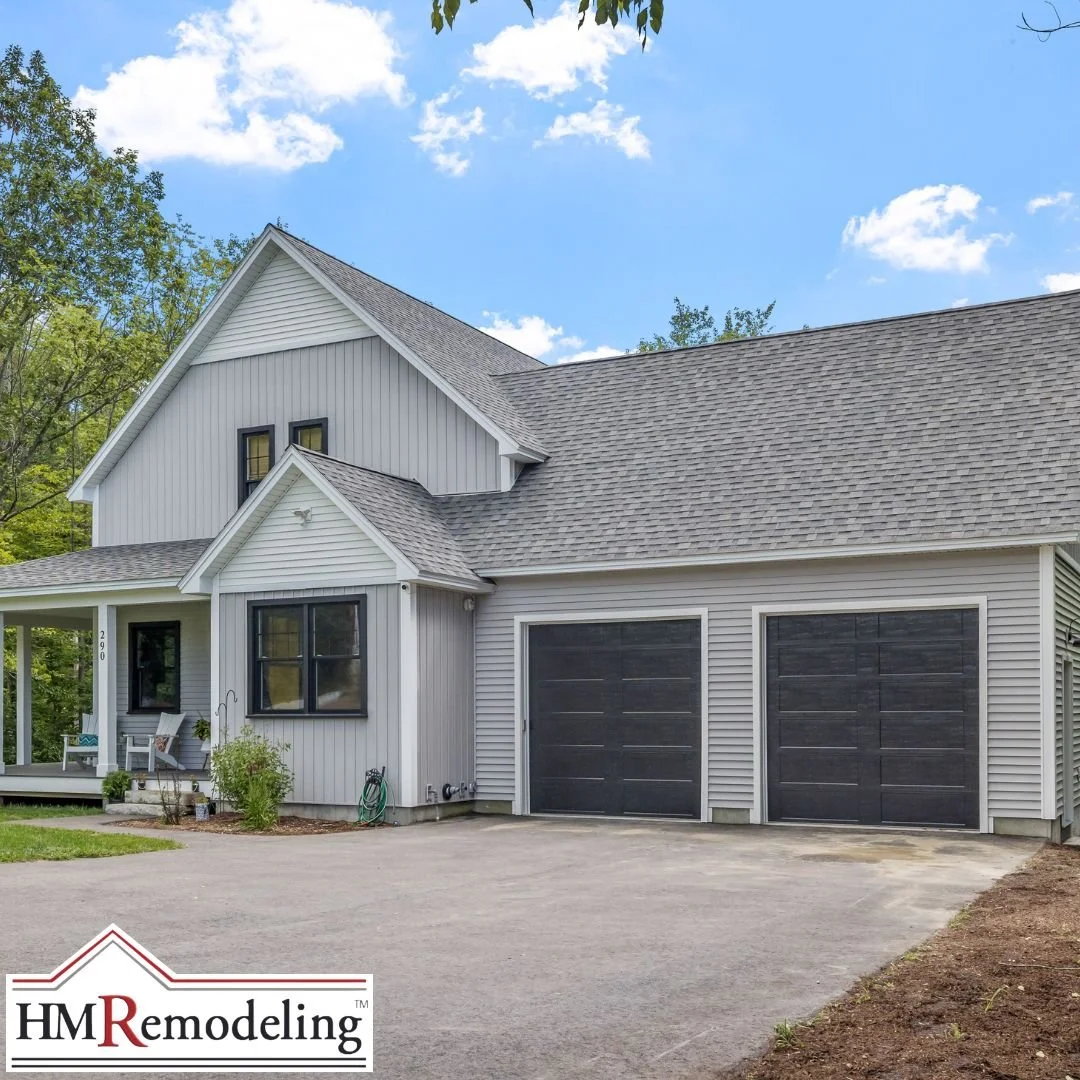 Modern farmhouse exterior with gray board and batten vertical siding, dark charcoal garage doors, black window trim, covered front porch, and concrete driveway on a South Bend, Indiana home remodeled by HM Remodeling