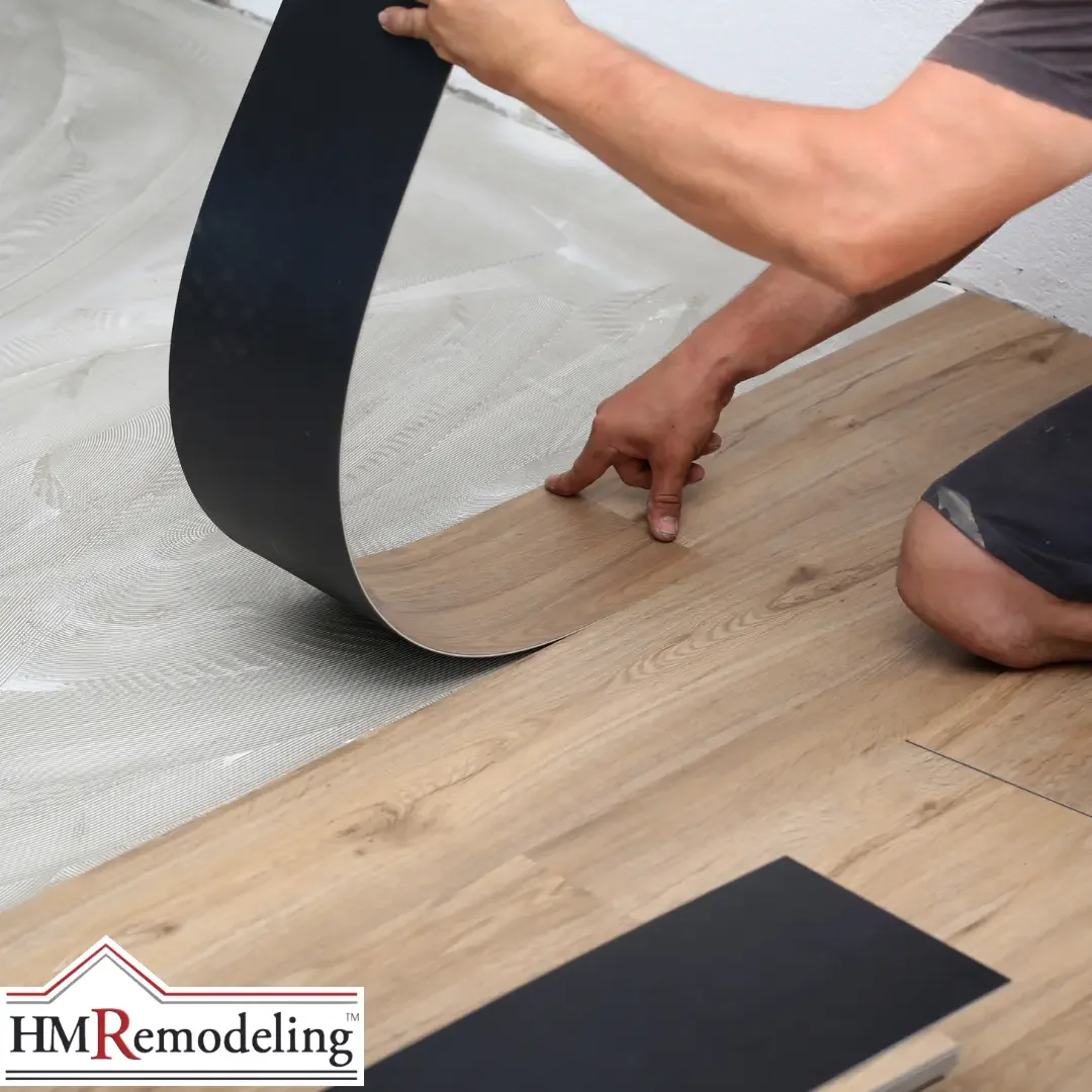 A installer kneeling on the floor peeling back a luxury vinyl plank tile to lay it onto an adhesive-coated concrete subfloor in a South Bend, Indiana home, with additional planks staged nearby