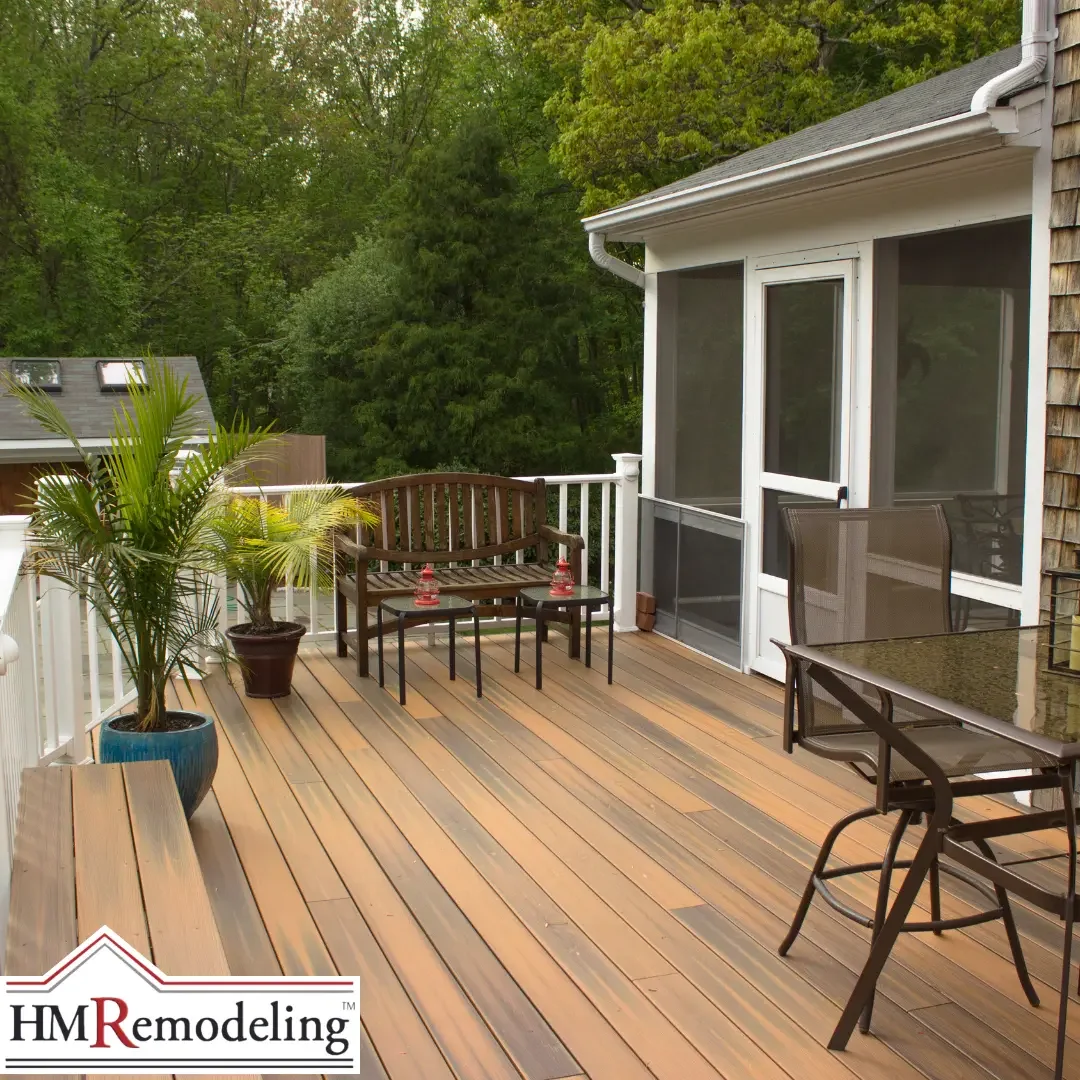 A composite wood deck with a bench, potted palms, and patio furniture beside a screened porch and wooded backyard at a Michiana area home.