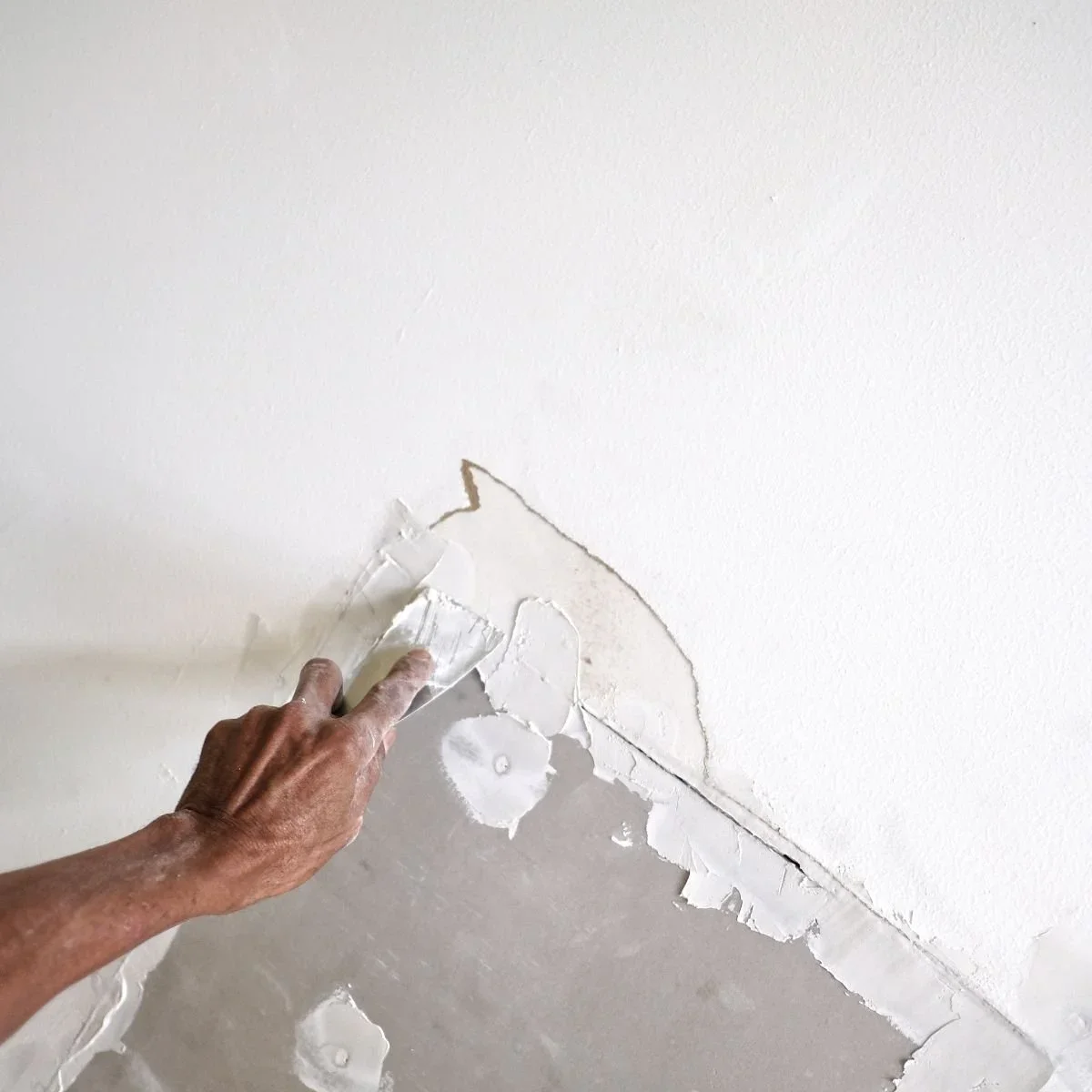 Professional drywall repair with contractor applying joint compound to patch damaged wall surface with putty knife by HM Remodeling in South Bend, Indiana
