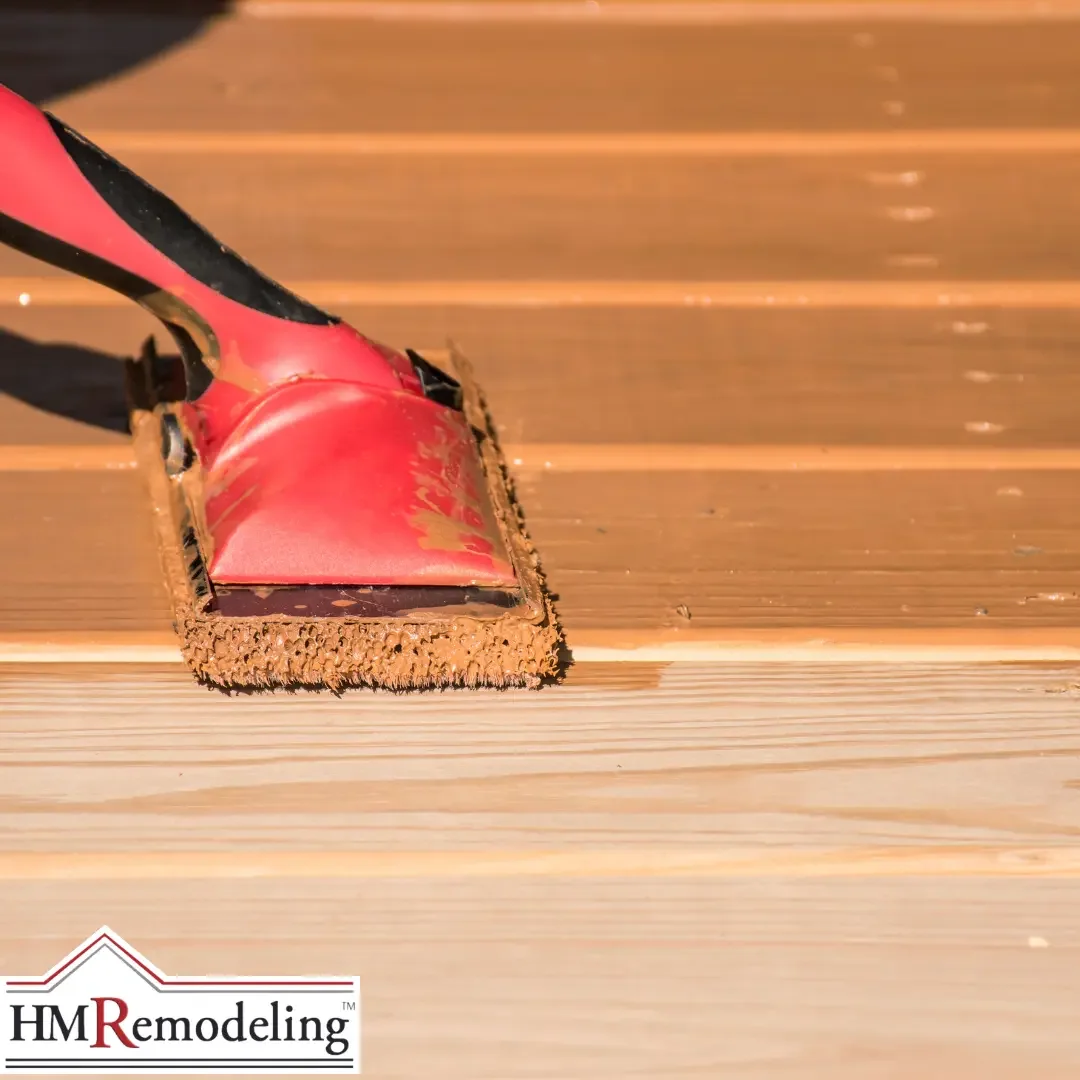 A red staining pad applying fresh penetrating stain to clean wood deck boards in a Michiana area backyard.