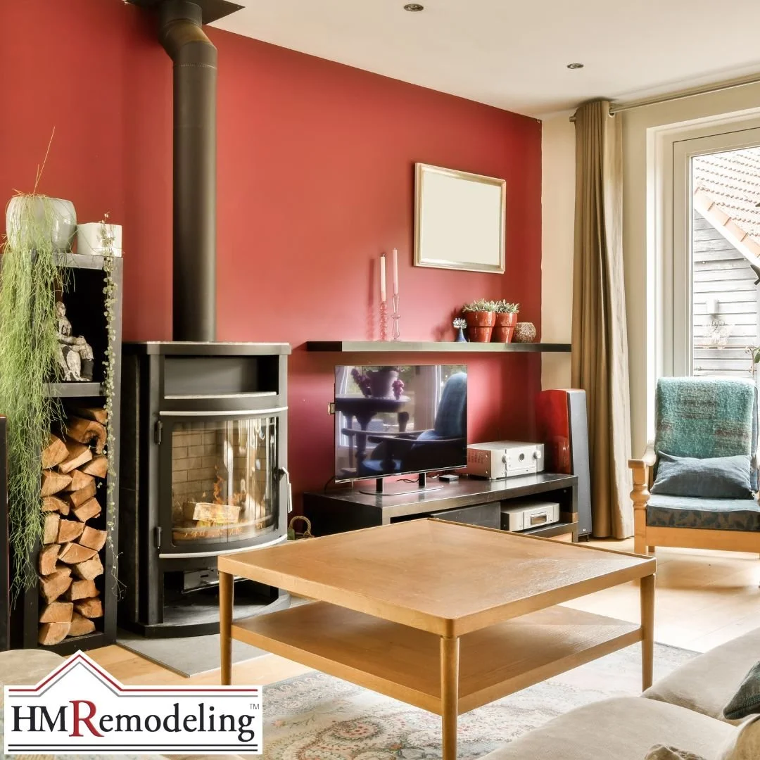 Living room interior paint refresh featuring a bold red accent wall, freestanding wood stove with firewood storage, wood coffee table, and large window with natural light in a South Bend, Indiana home