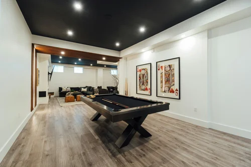 Finished basement renovation by HM Remodeling in South Bend Indiana featuring pool table lounge area, LVP flooring, black accent ceiling, and open living space